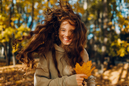 Smiling young woman enjoys the autumn season in the forest with the yellow leaves at sunsetの写真素材