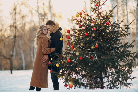 Young adult couple man and woman decorates pine tree in winter park forest. New year tree holiday party celebration conceptの写真素材