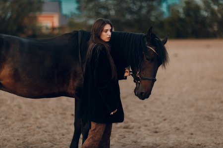 Young woman in black with her horse at sunset outdoorsの写真素材