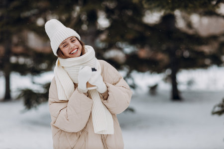 Happy smiling young woman with coffee hot drink cup enjoys winter weather at snowy winter parkの写真素材