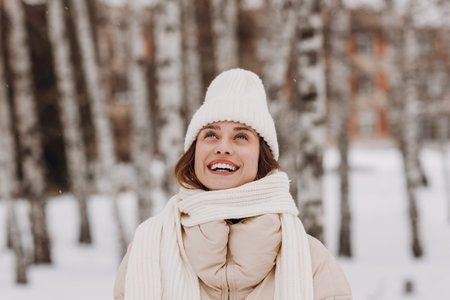 Young smiling woman dressed coat scarf hat and mittens enjoys winter weather at birch winter parkの写真素材