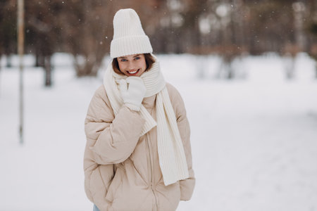 Young woman dressed coat scarf hat and mittens smiles and enjoys snowy winter park.の写真素材