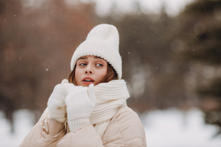 Young woman dressed coat scarf hat and mittens freezing winter weather at snowy winter parkの写真素材