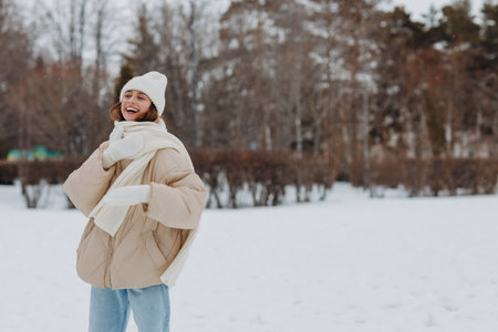 Happy smiling young woman portrait dressed coat scarf hat and mittens enjoys winter weather at snowy winter parkの写真素材