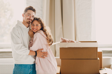 Happy young family couple man and woman hugging after moving cardboard boxes to their new apartment.の写真素材