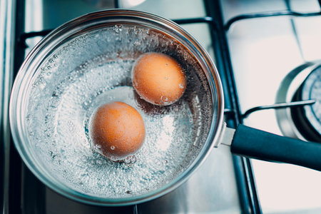 Saucepan stainless steel with two boiling eggs breakfast in a water on a gas stove top view.の写真素材