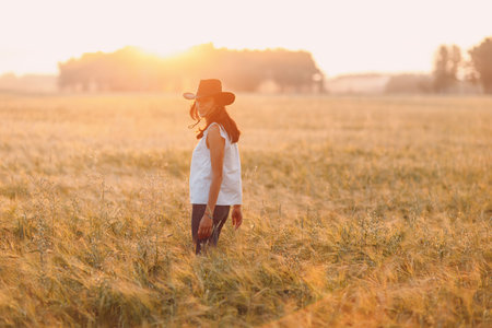 Woman farmer in cowboy hat at agricultural field on sunset.の写真素材