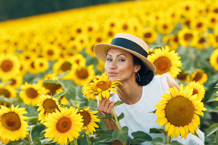 Beautiful young woman in a hat on a field of sunflowersの写真素材