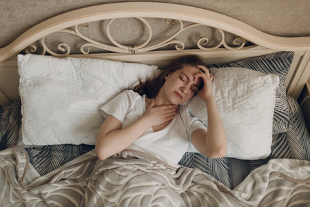 Young woman with headache flu ill sick disease cold at home indoor lying on bedの写真素材