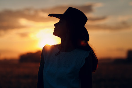 Woman farmer silhouette in cowboy hat at agricultural field on sunset.の写真素材