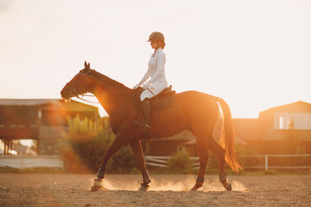 Woman rider jockey in helmet and white uniform preparing horseの写真素材