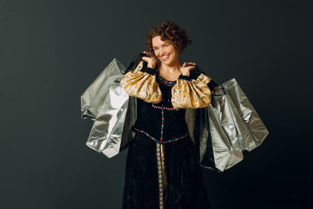Portrait of a young adult woman dressed in a medieval dress holding shopping bags in handsの写真素材