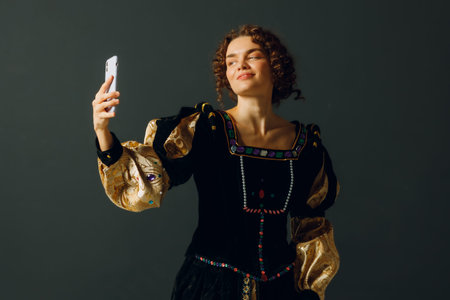 Portrait of a young aristocratic woman holding mobile phone dressed in a medieval dress on dark background