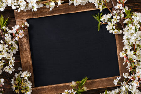 Old blank vintage school slate or chalkboard lying on an old rustic wooden background with dainty white flowers in two corners ready for your text or messageの写真素材