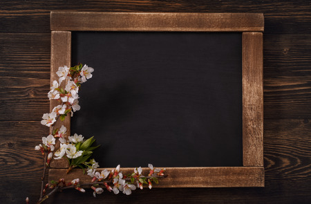Old blank vintage school slate or chalkboard lying on an old rustic wooden background with dainty white flowers in two corners ready for your text or messageの写真素材