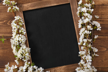 Old blank vintage school slate or chalkboard lying on an old rustic wooden background with dainty white flowers in two corners ready for your text or messageの写真素材