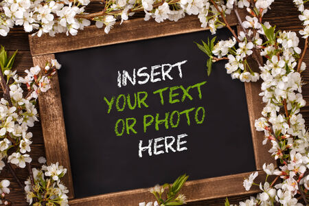 Old blank vintage school slate or chalkboard lying on an old rustic wooden background with dainty white flowers in two corners ready for your text or messageの写真素材