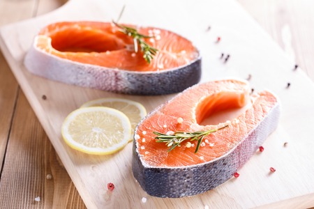 Salmon steak on wooden cutting board with herbsの写真素材