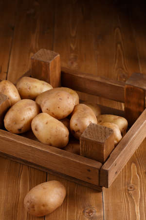 Potatoes in a wooden box on a wooden backgroundの写真素材