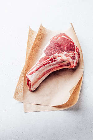 Raw rib eye on bone or cowboy steak on craft paper sheet. Top viewの写真素材