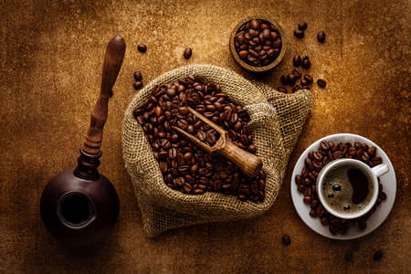Coffee grunge background. Vintage copper turkish coffee pot, roasted coffee beans in burlap sack and aromatic hot drink in cup top view flat layの写真素材