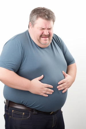 studio shot of a man holding his stomach in pain against a white backgroundの素材
