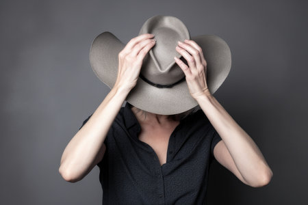 studio shot of an unrecognizable woman posing with a cowboy hat against a gray backgroundの素材