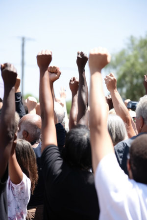 shot of a group of unidentifiable people holding their fists in the air outsideの素材