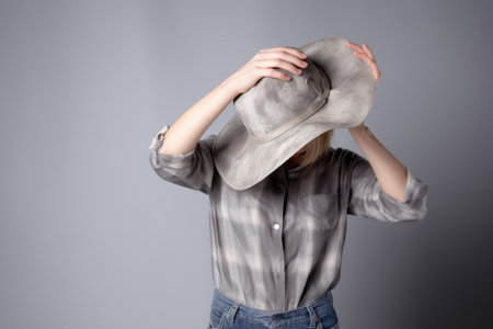 studio shot of an unrecognizable woman posing with a cowboy hat against a gray backgroundの素材