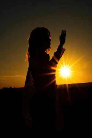 silhouette of a woman standing in front of the sun holding up her handの素材
