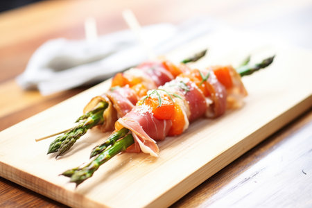 close-up of char-grilled prosciutto-wrapped asparagus on a rustic wooden boardの素材