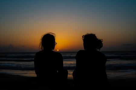 two silhouettes against sunset, on a quiet beachの素材