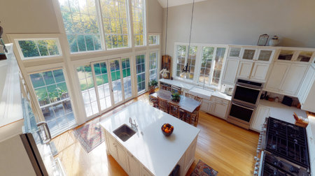 A birds-eye view of a spacious modern kitchen featuring a large white countertop island, gleaming stainless steel appliances, and oversized windows opening to a patio.の素材