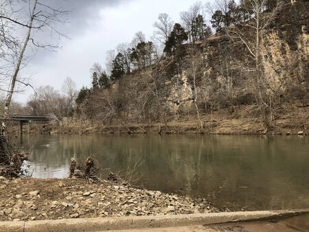 A murky river in the winter, surrounded by grey rocks and barren trees.の写真素材