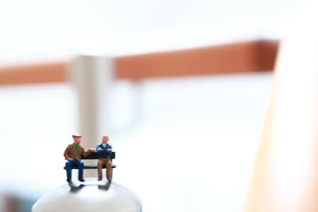Miniature retired people sitting on a bench and having conversation.