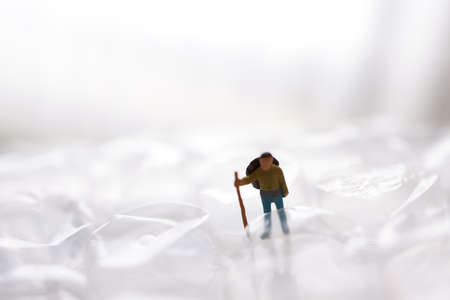 Miniature people: A man with a stick stands on a white sheet of paper.の写真素材