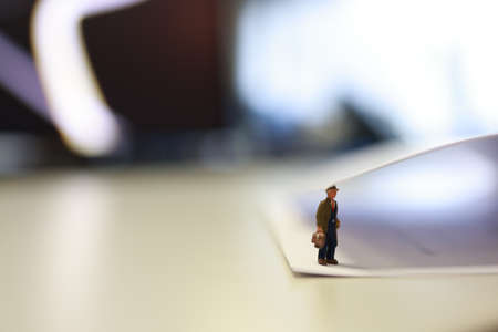 Miniature business people under a sheet of envelope paper in real office.