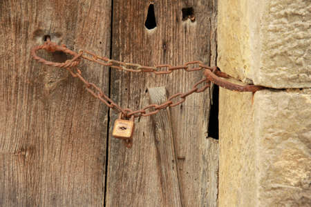 Old wooden door with rusty padlock and chain. Close up.
