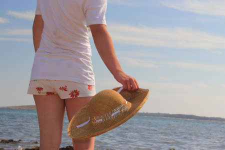 Girl with a straw hat on the beach. Back view. Selective focus.