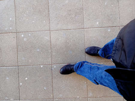 Close-up of a man's feet in blue jeans and a black baseball cap on the pavement