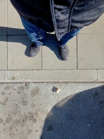 A vertical shot of a man wearing jeans and boots standing on the sidewalk