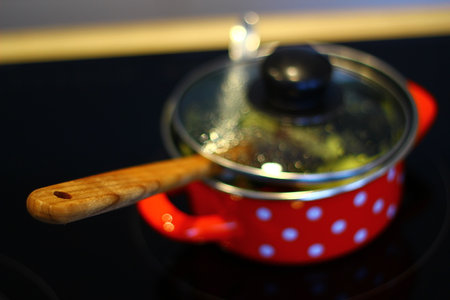 Red saucepan with wooden handle on the kitchen stove. Selective focus.の写真素材
