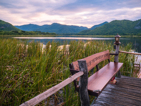 Sunrise over the lake in the village with the chair on the bridge. View from a wooden bridge, image in the Green-purple toning.の写真素材