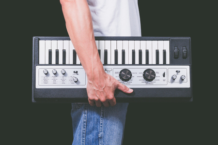 man holding vintage studio keyboard synthesizer, isolated on black for music background