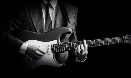 male musician in suit playing electric guitar, black and white. isolated on blackの写真素材