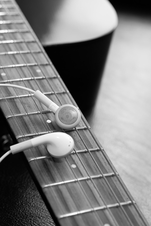 white earphones on acoustic guitar fingerboard for music background