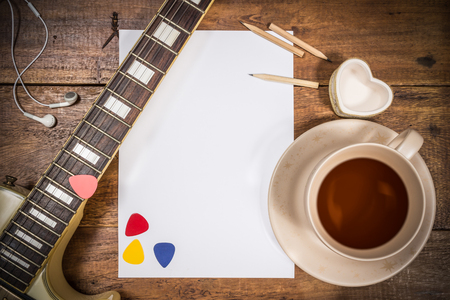 electric guitar, blank white paper & a cup of tea on wooden tableの写真素材