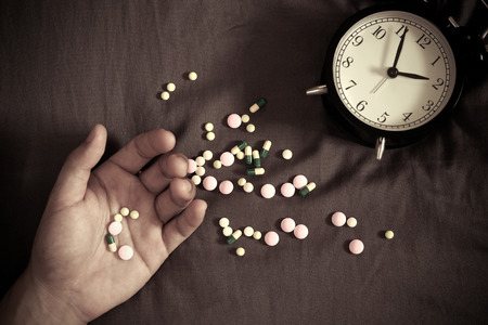man hand and drugs, tablets suffering insomnia, hangover, headache, overdose on bed at nightの写真素材