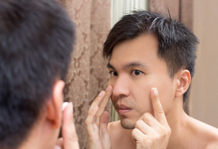 Mirror reflection of a young asian handsome man applying facialの写真素材