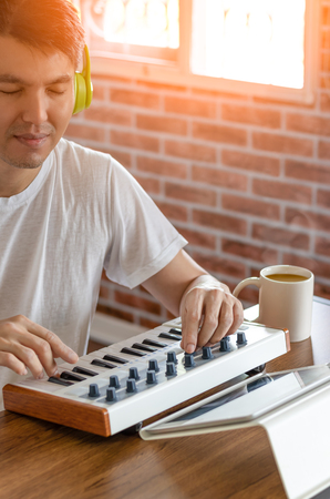 young asian handsome man enjoy playing music keyboard with tablet computer for relaxation in living room. composer making music in bedroom studioの写真素材